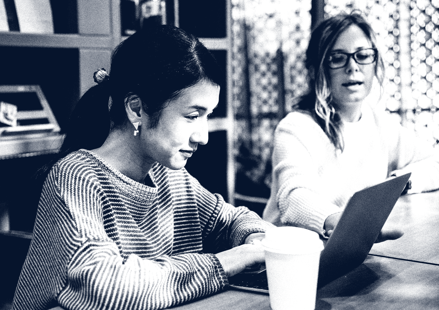 Two women looking at a laptop and discussing how much money they have saved since becoming Merchant Financial Group clients.